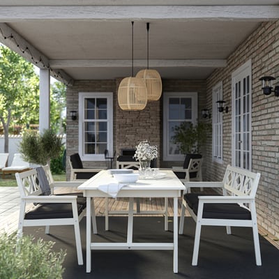 Moderne porcelæn spisebordssæt på muret veranda, med kurvelys, fade og blomster, på sort tæppe, udsigt til haven.