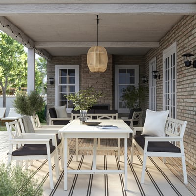 Udendørs spisebordssæt: akaciebord og stole, mørke puder, planteindretning, fredeligt.