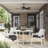 Hyggelig terrasse med hvide BONDHOLMEN udendørsmøbler sat under en sort loftsventilator på murstenshus, herunder et rundt spisebord og polstrede stole.