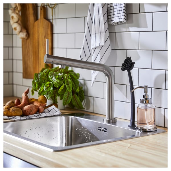 Moderne køkkenarmatur med finish i rustfrit stål, slankt design og håndtag på toppen. Grøntsager og sæbedispenser i nærheden.