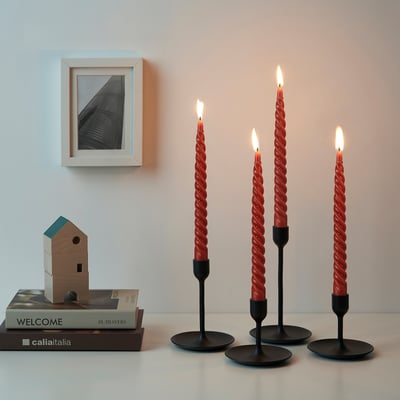 Fire tændte stearinlys i sorte holdere på en hvid overflade, med bøger og et træhusornament i nærheden; Et indrammet foto hænger ovenover.