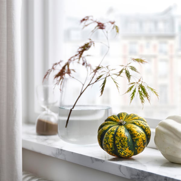 Vindueskarm med gulgrønne og hvide græskar og en klar vase med grene.