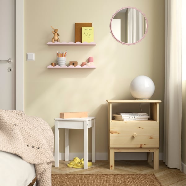 Hyggeligt hjørne: blødt lyserødt spejl over natbord i træ, lampe, bøger, lyserødt tæppe, enlig gul sko.