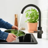 Person vasker broccoli i køkkenvask under sort DELSJÖN vandhane med høj tud.