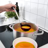 Madlavning suppe på komfur med øse, skål og urteplante.