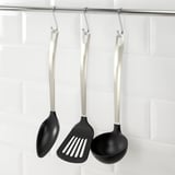 Tre sorte køkkenredskaber med sølvhåndtag hænger fra kroge: ske, spatel og øse, designet til non-stick gryder og pander.