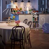 Moderne spiseplads med hængende lamper, blomster og vaser på bordet, tilstødende hyggeligt køkken med trægulve.