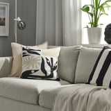 Moderne stue med grå sofa, dekorative puder, sort og hvid DRABOR pude, grøn plante, abstrakt skulptur, beige plaid