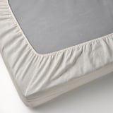 Et nærbillede af et hvidt stræklagen i 100 % hør med elastikkanter, der er designet til at passe til madrasser op til 36 cm tykke.