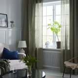 Moderne stue med store grågrønne DYTÅG hørgardiner, en stilfuld sofa og en hyggelig stol.