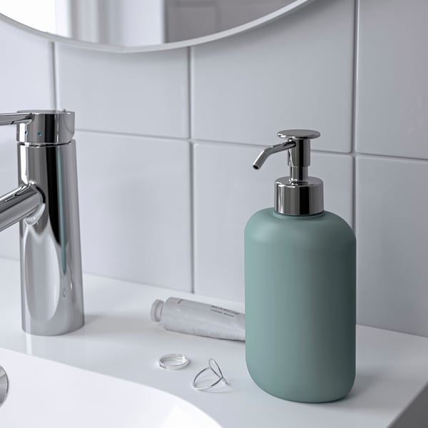 Moderne badeværelsesdisk med grøn EKOLN sæbedispenser, metallisk vandhane, cremefarvet rør og glas.