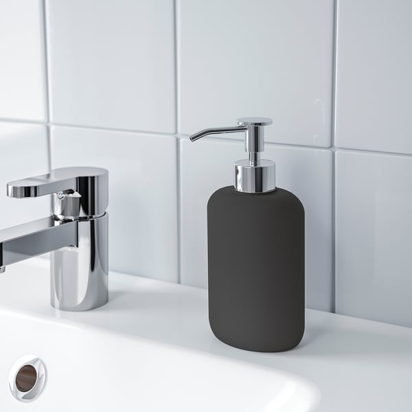 Sort sæbedispenser med metallisk pumpe på en hvid vask, en del af EKOLN-serien for et moderne badeværelseslook.