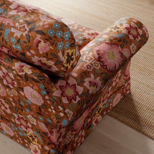 Blomstret lænestol nærbillede: indviklede, farverige blomstermønstre på varmt brunt stof, der udstråler komfort og elegance.