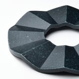 Mørk tekstureret cirkulær fod med geometrisk design, lavet af komprimeret bambus, der beskytter overflader og tilføjer moderne indretning.