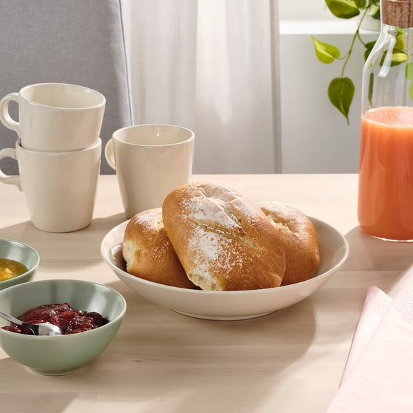 Skål med brød. Kopper, juice og marmelade på bordet.