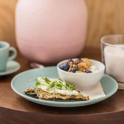 Et stilfuldt måltid bestående af frittata og frugt på FÄRGKLAR turkis tallerken, lyserøde og klare krus ved siden af på et træbord.