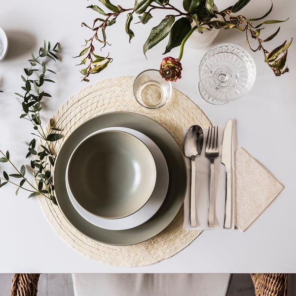 Elegant borddækning med FÄRGKLAR tallerken, grønt, sølvtøj, glas, hvid serviet.