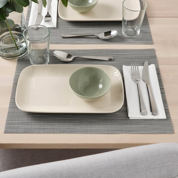 Borddækning med FÄRGKLAR skål, tallerkener, bestik og glas på dækkeservietter.