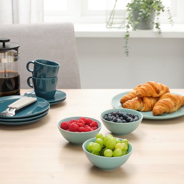 Blå borddækning med frugt, kaffe og kager nær et vindue.