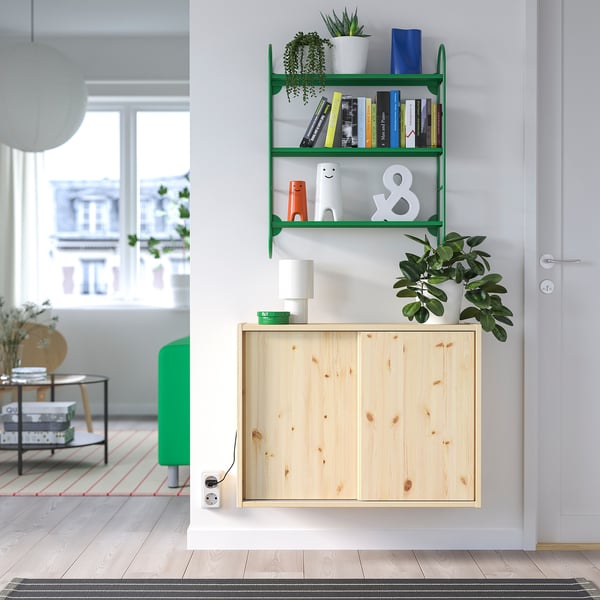 Moderne væghylde med bøger, indretning og planter; træskab nedenunder; nærliggende vindue og skammel.