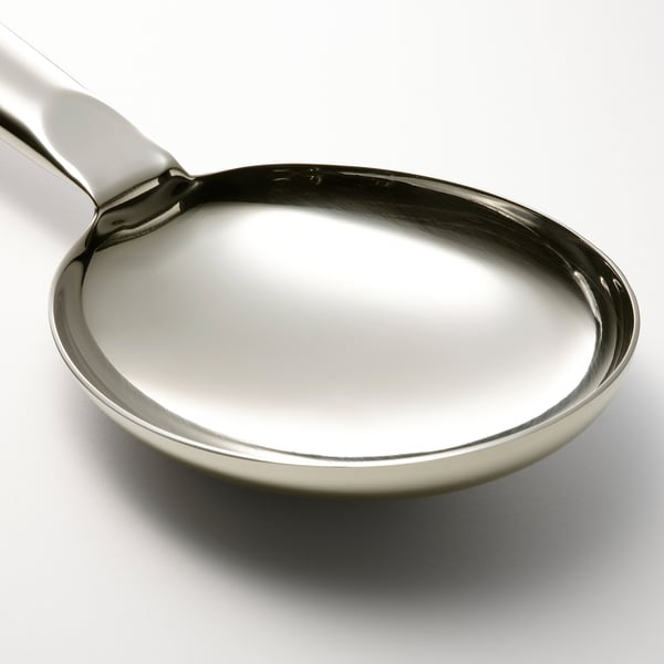 Ske i rustfrit stål med buet håndtag og dyb skål, designet til omrøring og servering, vist med en skyggefuld hvid baggrund.