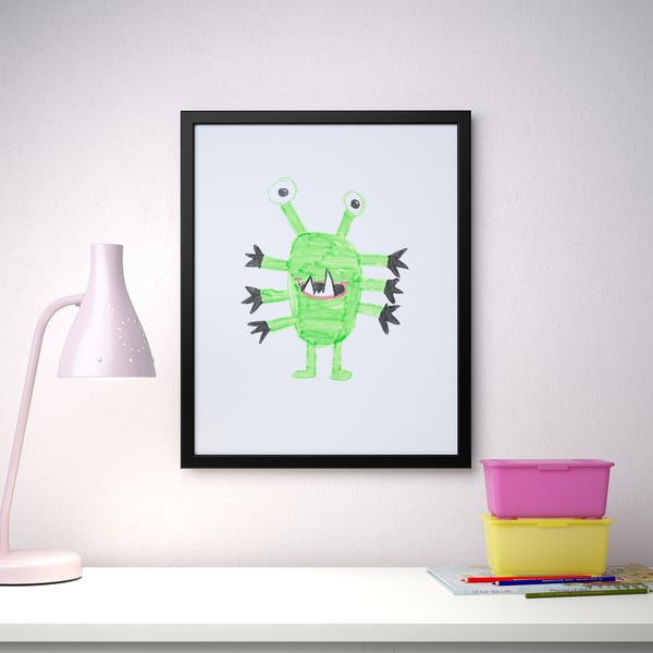 Indrammet grøn monsterkunst med en lampe og opbevaringsbokse på et hvidt skrivebord.