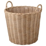 En rund FLODBJÖRK vævet kurv i beige. Den er håndlavet af slidstærkt plastrattan, designet til både indendørs og udendørs brug, med to håndtag på toppen.