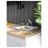 Moderne køkkenvask i rustfrit stål, installeret i bordplade i træ, med en tallerken salat.