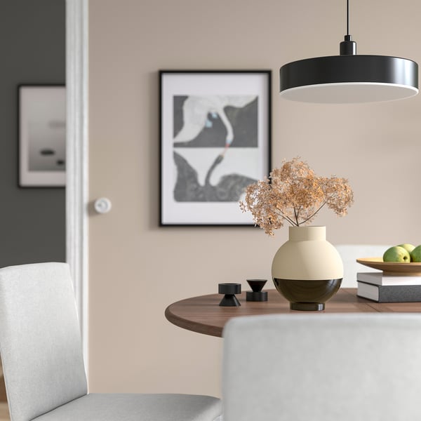 Moderne spisebord med sort og beige vase, tørrede blomster, små lysestager, grønne æbler, pendel og abstrakt vægkunst.