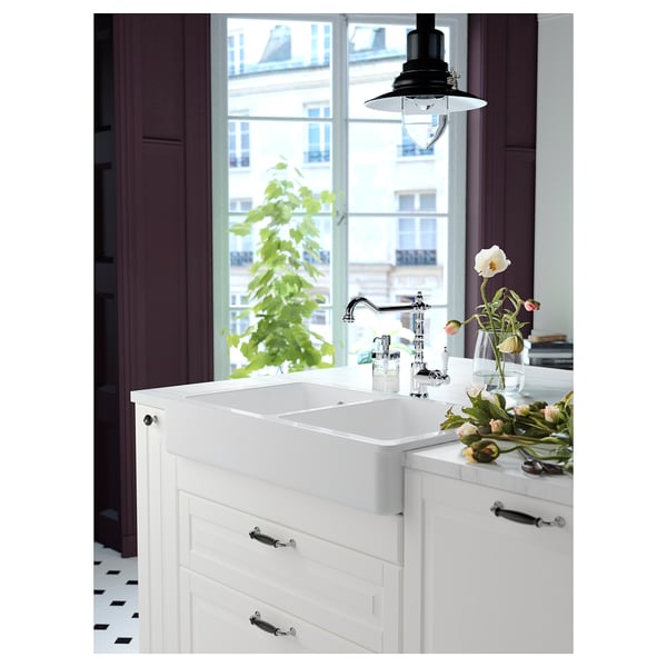 Moderne køkken med hvide skabe, krom vandhane, vinduesudsigt, blomster, sorte håndtag.