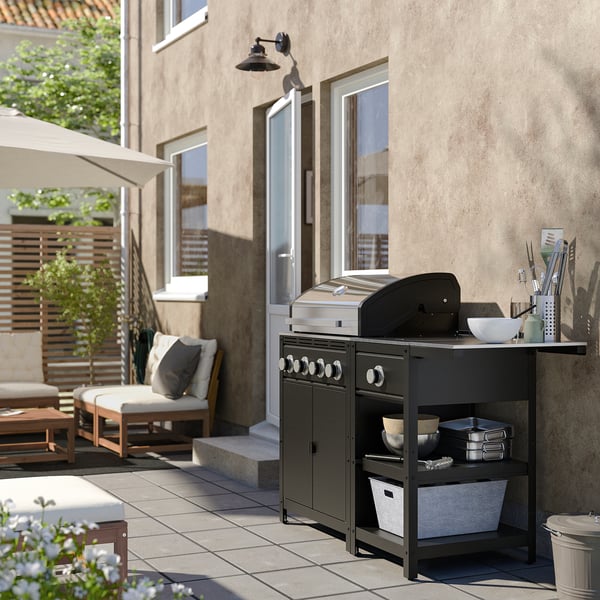 Moderne udekøkken med sort GRILLSKÄR gasgrill og sidebrænder, omgivet af beige arkitektur og møbler.