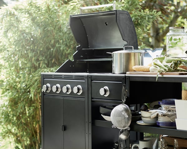 Udekøkken med sort GRILLSKÄR grill, tilbehør i rustfrit stål og grønne planter.