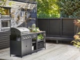 Et moderne udekøkken med en sølvfarvet gasgrill og sorte opbevaringsenheder på en træterrasse, der giver rigelig plads til madlavning og forberedelse.
