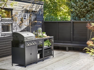 Et moderne udekøkken med en sølvfarvet gasgrill og sorte opbevaringsenheder på en træterrasse, der giver rigelig plads til madlavning og forberedelse.