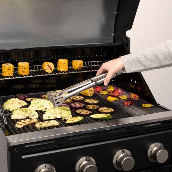 Person, der griller grøntsager ved hjælp af GRILLTIDER-redskaber på en gasgrill.