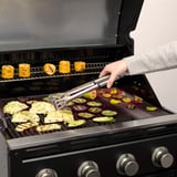 Person, der griller grøntsager ved hjælp af GRILLTIDER-redskaber på en gasgrill.