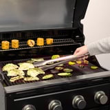 Person, der griller forskellige grøntsager ved hjælp af en tang på en moderne gasgrill.