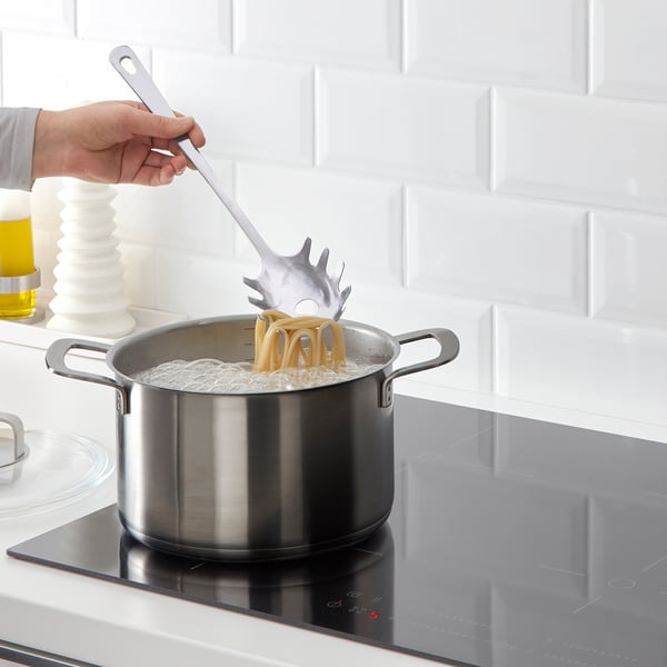 Person, der koger pasta ved hjælp af en spaghettiserver på et komfur.