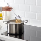 Person, der koger pasta ved hjælp af en spaghettiserver på et komfur.