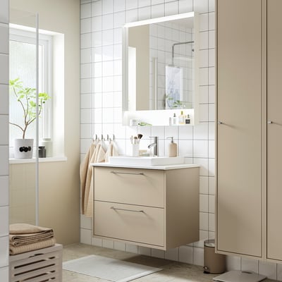 Moderne badeværelse med cremefarvet sminkebord, spejl, hvid vask, håndklæder, plante, vindue.