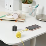 Et pænt arbejdsområde med en telefon, der oplades via et gult HAVSKÅL usb-anker for at holde kablet ryddeligt.