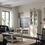 Moderne stue med lyst træ-tv-møbel, bogreol og mørk sofa. Fladskærms-tv, sofabord, gardiner og vægdekorationer.