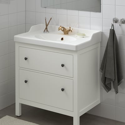Hvid HEMNES badeværelsesvask, to store skuffer, enkelt skålvask, guldhane, hængende gråt håndklæde.