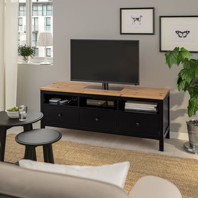 Sort HEMNES tv-stativ i fyrretræ, lavt med 3 skuffer, tv, plante, vindue, sofa.