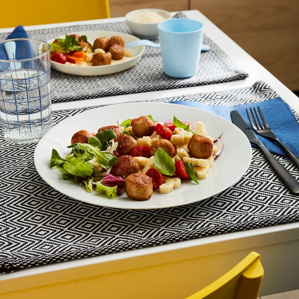 Et måltid med kyllingefrikadeller, salat og en drik på et bord med blå og hvide kuverter.