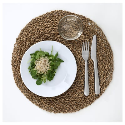 En hvid tallerken med grøn salat, glas og redskaber på vævet dækkeserviet.