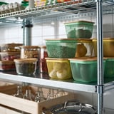 Metalhylder med grønne netkurve og trælåg med frugt og grøntsager, klare krukker med korn og glasflasker med propper.