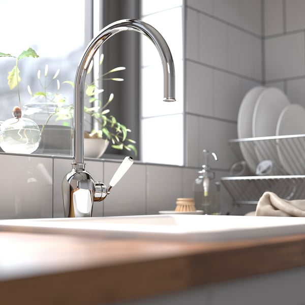 Moderne køkkenvask med krom INSJÖN vandhane. Slankt, buet design, skinnende metal. Høj, effektiv, omgivet af rene tallerkener, planter, sæbe.