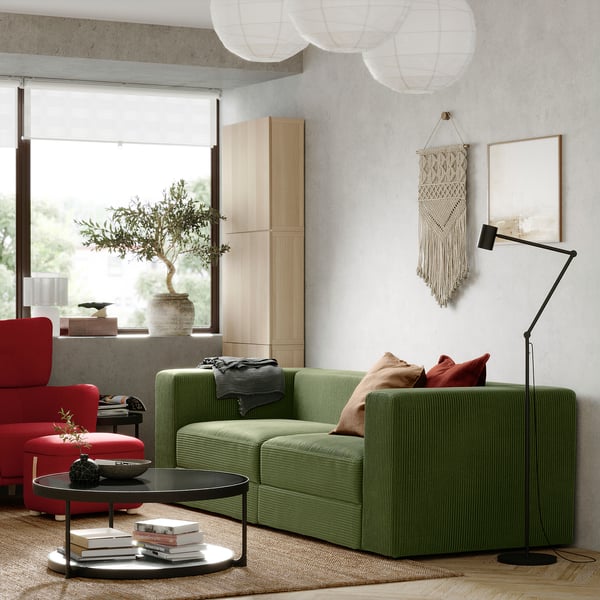 Moderne stue med olivengrøn JÄTTEBO sofa, røde stole, træskabe og gulvlampe.