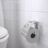 En moderne toiletpapirholder i krom på en flisebelagt væg, der holder en rulle toiletpapir sikkert.